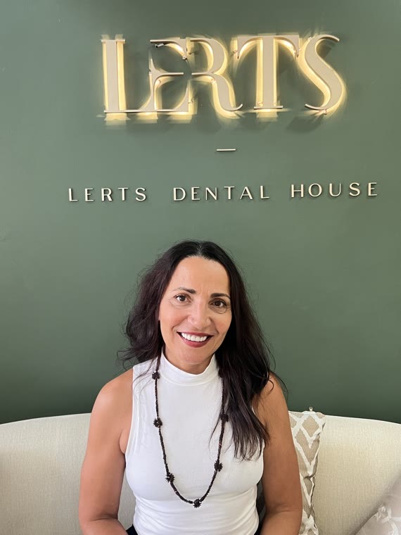 Patient smiling at the Dental Excellence logo wall, Chiang Mai